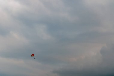 Parlak kırmızı bir paraşütün altında sürüklenen yalnız bir paraşütçü engin, dramatik bulutlu gökyüzüne karşı sessiz bir kıyı ufkunun üzerinde özgürlük, macera ve yalnızlığı çağrıştırıyor..