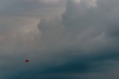 Parlak kırmızı bir paraşütün altında sürüklenen yalnız bir paraşütçü engin, dramatik bulutlu gökyüzüne karşı sessiz bir kıyı ufkunun üzerinde özgürlük, macera ve yalnızlığı çağrıştırıyor..