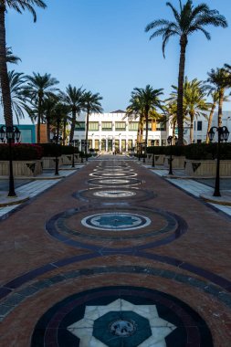 Güneşli bir palmiye bahçesi geçidi, dairesel mozaik kaplamaları, uzun lambalar ve sakin ve zarif bir tatil atmosferi yaratan tropikal peyzajların yer aldığı beyaz bir tatil merkezine götürür. Doha, Katar