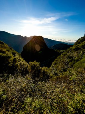 Portekiz 'in Madeira Adası engebeli dağ manzarasının üzerinde dramatik bir gün doğumu. Güneş ışınları zirveleri aşıyor ve yemyeşil vadiyi ve volkanik tepeleri aydınlatıyor. Atlantik adasının vahşi doğasında nefes kesici bir doğa manzarası yaratıyor..