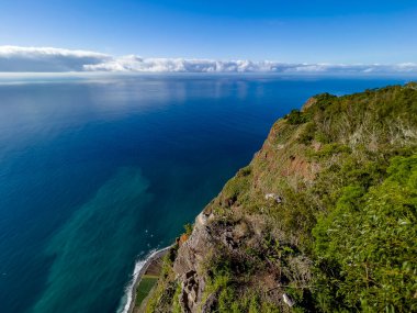 Portekiz 'in Madeira Adası' ndaki derin mavi Atlantik Okyanusuna düşen sarp yeşil kayalıkların nefes kesici manzarası dramatik kıyı manzaralı güneşli bir günde çekildi..