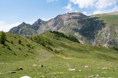 Yeşil tepeleri ve mavi gökyüzünün altındaki kayalık tepeleri olan dağlık bir manzaranın manzarası..