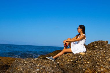 Güneşli bir günde Sahildeki Kayalıklarda Beyaz Elbiseli Kadın pozu