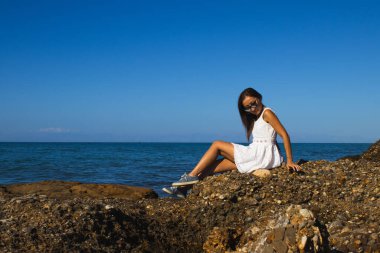 Güneşli bir günde Sahildeki Kayalıklarda Beyaz Elbiseli Kadın pozu