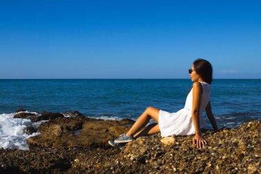 Güneşli bir günde Sahildeki Kayalıklarda Beyaz Elbiseli Kadın pozu