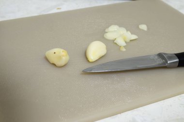 Açık Bej Kesme tahtasında Soyulmuş Sarımsak ve Keskin Bıçak