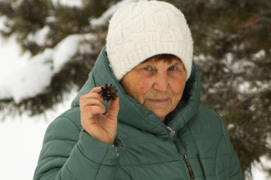 Yeşil Kış Ceketli Kıdemli Kadın Küçük Çam Kozalağı Tutuyor