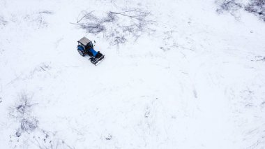 Kırsal kesimdeki karla kaplı arazide mavi traktör sürüyor.