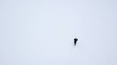 Uçsuz bucaksız bir kar tarlasında tek bir kros kayakçısının yüksek açılı hava görüntüsü