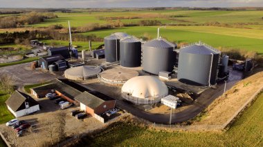 Danimarka 'da yeşil tarım arazileriyle çevrili büyük bir biyogaz üretim tesisinin insansız hava aracı görüntüsü yenilenebilir enerji altyapısı ve sürdürülebilir kırsal teknolojiyi vurguluyor.