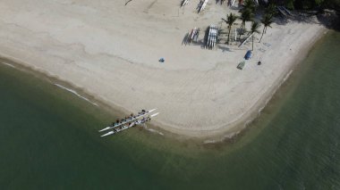 İnsansız hava aracı, Brezilya 'nın Angra dos Reis kentindeki tropikal beyaz kum plajına motorlu çift kano çeken insanların fotoğrafını çekiyor..