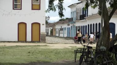 Charming Paraty Meydanı, ön planda bir ağaç, park edilmiş bisikletler, tipik bir koloni evi ve arka plandaki insanlar. Kasaba sakin, otantik atmosferi yakalar..