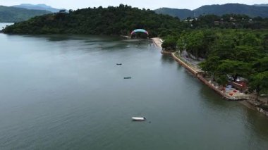 Paraty Körfezi 'nin ve Brezilya' nın Paraty kentindeki sık ormanlarla kaplı dağların çarpıcı manzarasıyla Jabaquara Sahili 'nde yüzen iki paraşütçü.