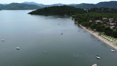 Paraty körfezi, küçük adalar ve Brezilya 'nın Paraty kentindeki yoğun Atlantik Ormanı ile kaplı dağlarla birlikte Jabaquara Sahili' nde yüzen ikili paraşütçüler.