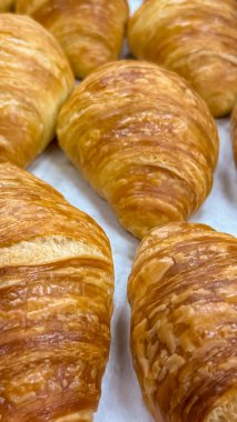 Sıcak ve davetkar bir sıra taze pişmiş kruvasan parşömen kağıdında soğuyor. Yumuşak ışıklandırma ve sığ alan derinliği taze ve lezzeti, kafe menüleri ve konukseverlik pazarlaması için ideal olanı vurguluyor..