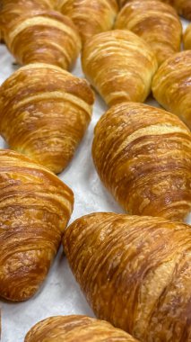 Taze bir parça el yapımı mini kruvasan yakın çekim. Resim, bir fırın vitrini için düzgünce düzenlenmiş el yapımı Fransız hamur işlerinin narin, tereyağlı tabakalarını ve mükemmel kahverengi kabuğunu sergiliyor..