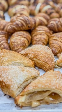 Fırından çıkan taze hamur işlerinin yemek fotoğrafları. Altın-kahverengi hamur işleri beyaz bir yüzeyde duruyor. Kabarık, katmanlı doku görülebilir, tereyağlı, puf böreği bileşimini gösteriyor. Kenarları biraz gevrek, bu da taze pişmiş olduklarını gösteriyor..