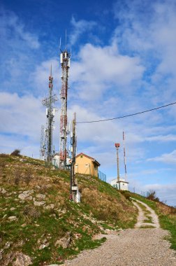 Derin mavi gökyüzü ve beyaz bulutlara karşı antenlerle iki iletişim kulesi