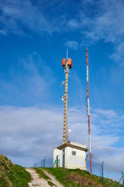 Derin mavi gökyüzü ve beyaz bulutlara karşı antenlerle iki iletişim kulesi