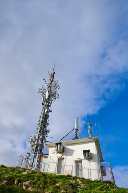Derin mavi gökyüzü ve beyaz bulutlara karşı antenlerle iki iletişim kulesi