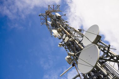 Derin mavi gökyüzü ve beyaz bulutlara karşı antenlerle iki iletişim kulesi