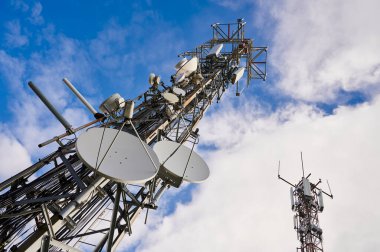 Derin mavi gökyüzü ve beyaz bulutlara karşı antenlerle iki iletişim kulesi