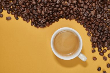 Sarı arka planda bir fincan kahve ve kahve çekirdeği.