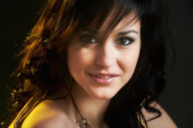 Siyah gözlü, güzel gülümseyen ve kameraya bakan güzel bir genç kadının portresi.