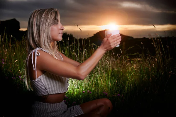 Sarışın kız gün batımında elinde mumla meditasyon yapıyor.