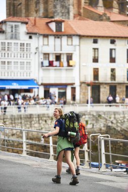 Geniş sırt çantalı genç bir kadın Avrupa kıyı kasabasında gezinti güvertesinde yürüyüş deneyiminin tadını çıkartıyor.