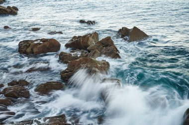 Dalgalar kayaların üzerinde uzun pozlama görüntüsüyle kırılıyor