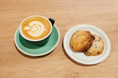 Tahta bir masada bir fincan kahve ve kurabiyeler.