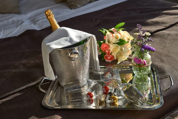 Şampanyalı bir şişe şampanyayla buz, çikolata ve iki bardak şampanyayla birlikte bir buket gülle yatakta.