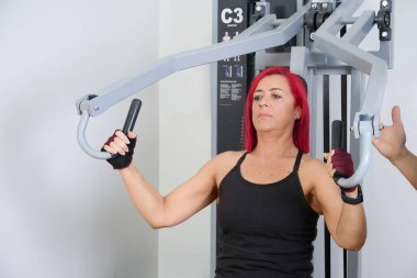 Kadın dayanıklılık antrenmanı yapıyor, göğüs ve kollarını spor makinesinde çalıştırıyor, fitness hedeflerine odaklanıyor.