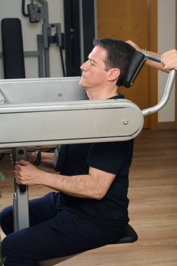Adam medikal spor salonunda rehabilitasyon, omurga bakımı ve kas güçlenmesi için rehberli boyun egzersizi yapıyor.