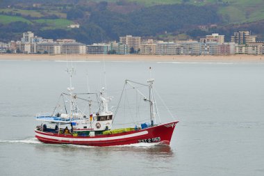 Balıkçı teknesi, binaları, plajı ve yeşil tepeleri olan kalabalık bir sahil şeridine doğru yol alıyor. Santona, cantabria