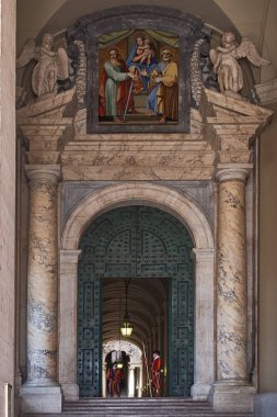 Geleneksel üniformalı İsviçreli muhafızlar, dini bir mozaiğin altında, Vatikan 'daki Aziz Peter Bazilikasının girişini koruyorlar.