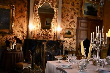 Kraliyet Sarayı oturma odasının içinde resmi olarak servis edilen bir yemek masası var. Zengin tarihi dekor ve sıcak tonlar aristokratik yaşam tarzını ve törensel yemek geleneğini yansıtıyor.