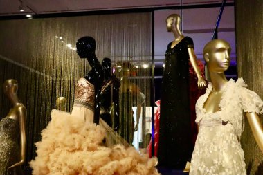 Fotoğrafta, altın ve bej tonlarında sahne kostümleri giymiş bir grup manken yer alıyor. Kıyafetler ışığı yakalamak için tasarlandı. Tiyatral bir zarafet hissi yaratıyor..