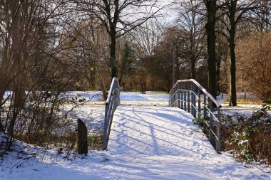 Karlı bir köprü, çıplak ağaçlarla çevrili bir parkın nehrinden geçer. Kış, sahneyi beyaza boyardı..