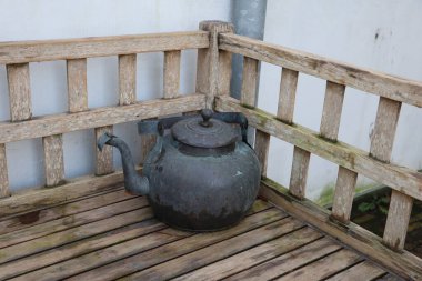 Parktaki ahşap bir bankta sergilenen eski bir metal çaydanlık müzelik bir nesneye benziyor..