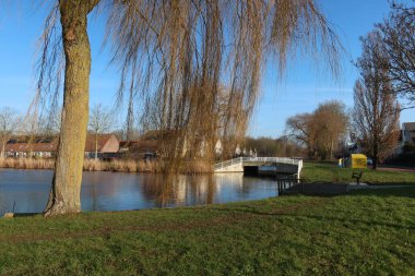 Güneşli bir günde beyaz bir köprüsü, evleri ve söğüt dalları olan kanal manzarası.
