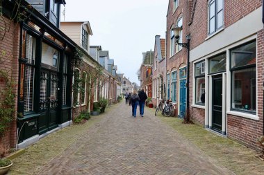 Alkmaar 'da dar bir sokakta insanlar yürüyor ve bisikletleri yan tarafa park ediyor. Sahne tipik bir Hollanda kentsel atmosferini yakalıyor.