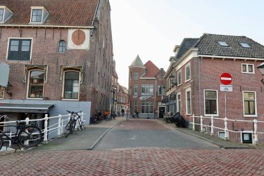 Bulutlu bir Alkmaar manzarası, küçük bir köprü, bisikletler ve geleneksel Hollanda evleri. Sahne, şehir hayatının sakin ritmini yakalar..