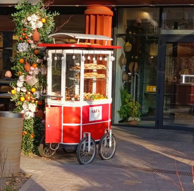 Noel için dekore edilmiş bir restoranın girişinde duran çeşitli hamur işleriyle seyyar fırın tezgahı. Sıcak ışıklar, tatil süsleri ve rahat mevsimlik atmosfer davetkar bir sokak yemeği sahnesi oluşturur..