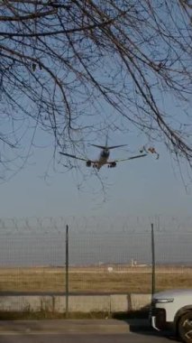 Alçaktan inmek için yaklaşan bir uçak bir araba ve bir motosiklet altından geçerken. Havacılık, trafik ve kentsel hareketleri bir çerçevede yakalayan dinamik bir sahne. 