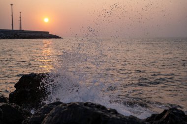Güneş doğarken dalgalar çarpar, kayalar altın ışığa püskürtür, kuş sürüsü uzak bacaların üstünde kıvrılır ve tüy çıkarır.