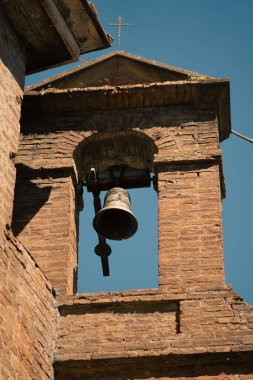 Gökyüzüne karşı çerçevelenmiş güneşli tuğla çan kulesi, yakından bakınca asılı zilli tuğla çan kulesini gösteriyor.
