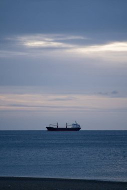 Sakin Okyanus Şafağında Şilep Silueti. Yumuşak Gündoğumu Öncesi Işık, Düşük Bulut Grubu, Ufuk Yakınındaki Yalnız Gemi, Sessiz Mavi Palet, Yansıtıcı Su, Minimalist Ruh hali, Seçici Odaklanma