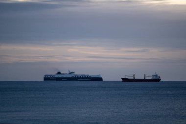 Kargo Gemisi Şafağı 'nın yanındaki yolcu feribotu. Beyaz Feribot ve Kırmızı Şilep Horizon, Katmanlı Bulutlar, Sahil Nakliye Yolu Yansıtıcı Su, Seyahat Kontrastı, Uzay Kontrastı